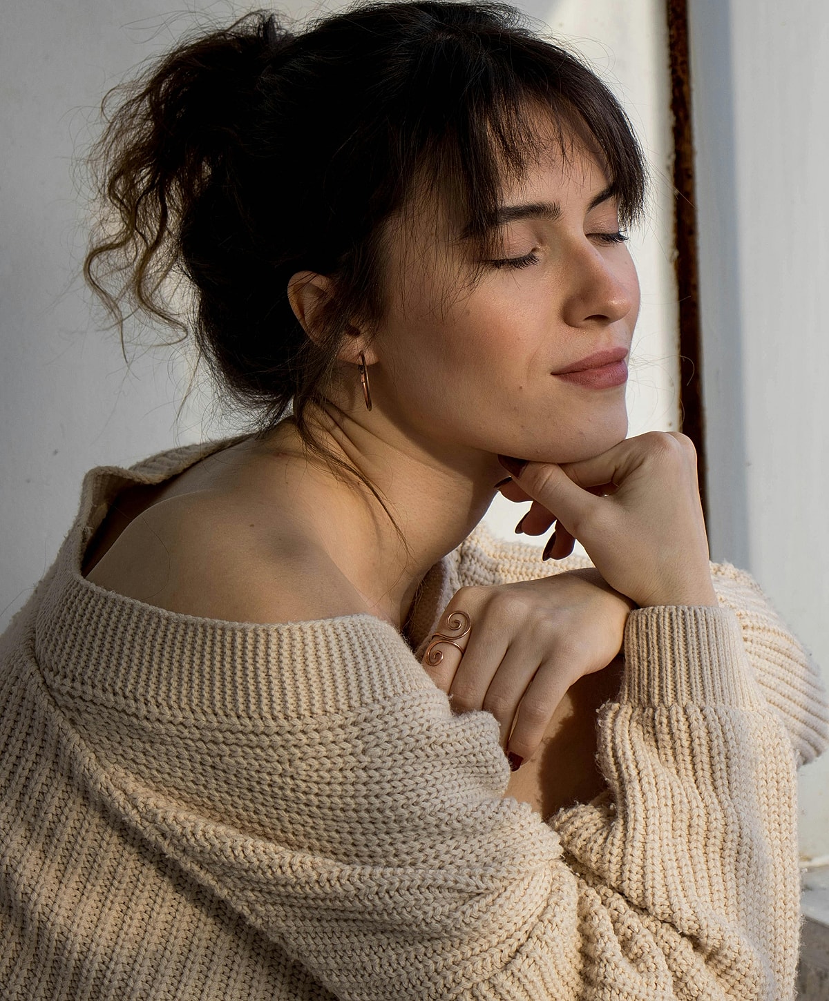Woman in cozy sweater, eyes closed, thoughtful expression.