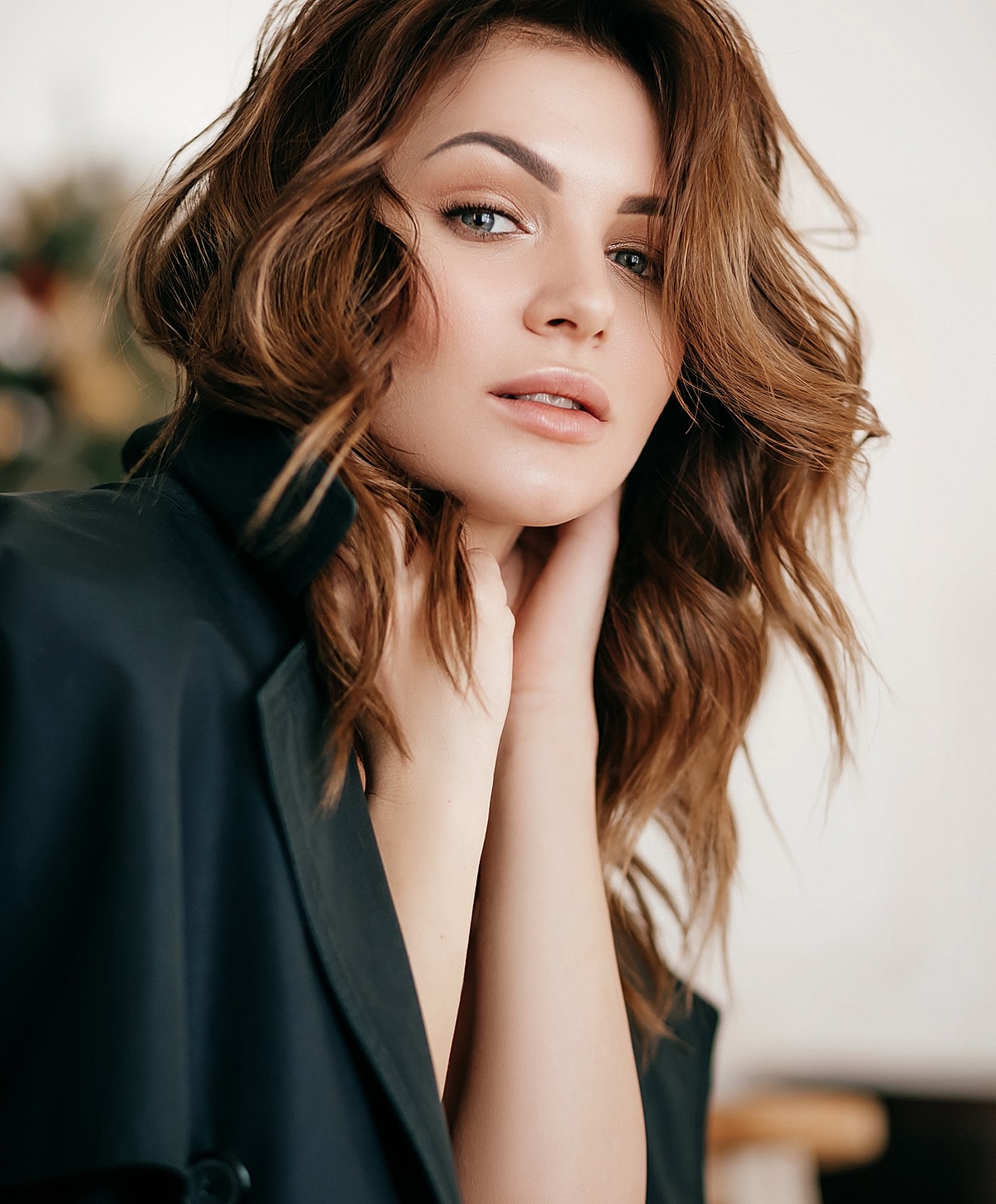 Woman with wavy hair, soft expression, dark coat.