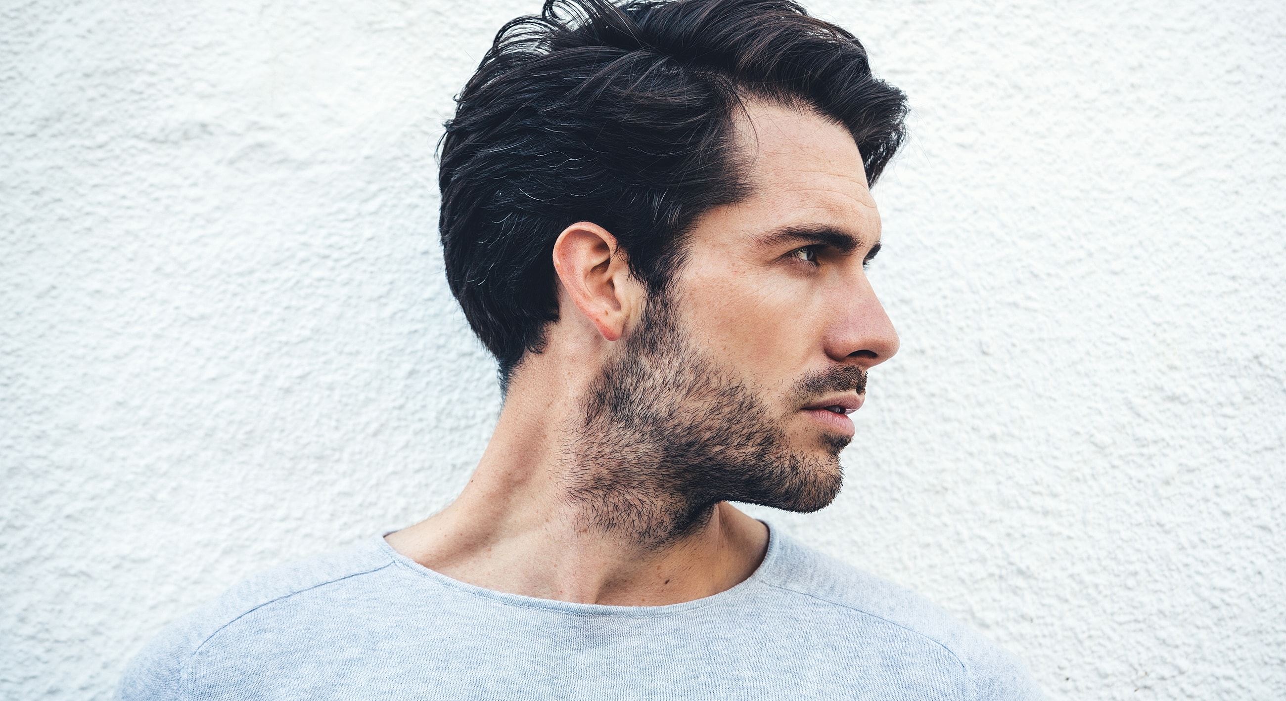 Man with stylish hair against a white wall.