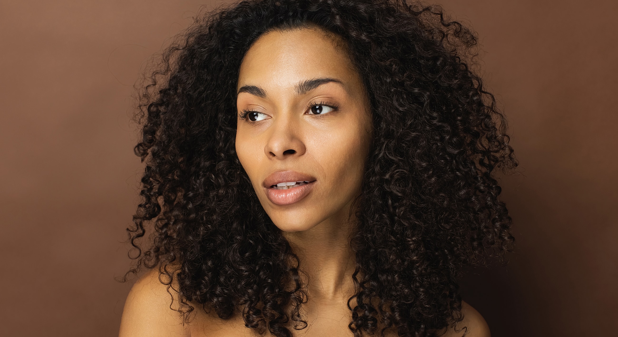Woman with curly hair against a brown background.